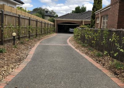 A winding driveway lined with greenery, leading to a garage beneath a house, under a partly cloudy sky.