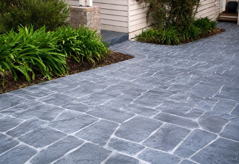 Residential textured concrete driveway featuring a natural stone pattern finish surrounded by landscaped gardens