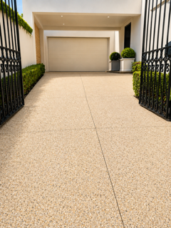 Light exposed aggregate concrete driveway leading to a modern residential garage with landscaped garden edging