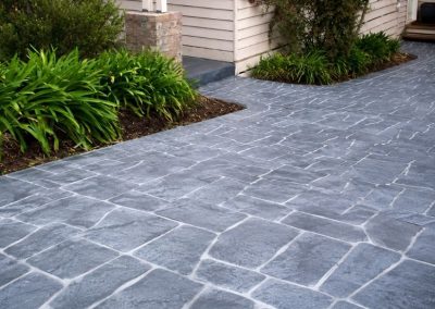 Slate grey textured concrete driveway with a natural stone pattern beside a landscaped home garden