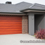 A Better Driveway Modern house with a wood garage door, brick wall, gray roof, and entryway with ornamental grasses.
