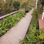 Residential garden path with greenery, deck, and house.