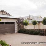 A Better Driveway A residential scene with two houses, featuring a large garage and small trees in the foreground, under an overcast sky.