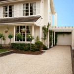 Exposed aggregate looks wonderful against virtually any style of home Two-story beige house with dark brown roof, driveway, and small front garden.