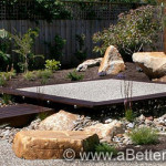 Stunning exposed aggregate nestled amongst beautiful landscape. A structured garden with gravel areas, boulders, and diverse plants.