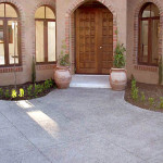 Lovely saw cut tile in exposed aggregate Entrance with a wooden door, arched windows, and terracotta plant pots on a textured concrete walkway.