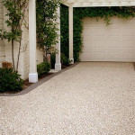 This blend is a combination of white and grey cement Driveway with a pebble surface under a white pergola, leading to a closed garage door.