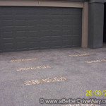 Modern exposed aggregate A dark gray garage door with a concrete driveway featuring embedded stone rows.