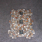 We can place pebble tiles like this as a feature Rectangular stone mosaic with dark green tiles set into a pebbly surface.