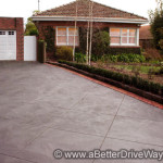 A suburban house with a gray concrete driveway, red brick garage, and hedges.