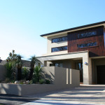 This stunning driveway in Brighton shows all of what exposed aggregate can be. Modern two-story house with concrete and wood facade, featuring a garden and garage.