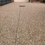 Exposed aggregate concrete driveway leading to a cream garage door
